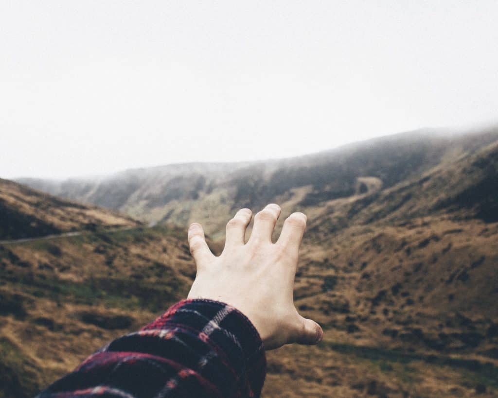 point of view photography of person raising hand towards mountains