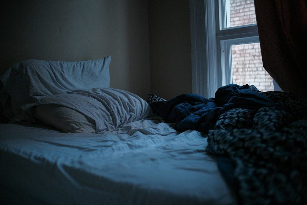 An unmade bed in a dark, quiet bedroom.